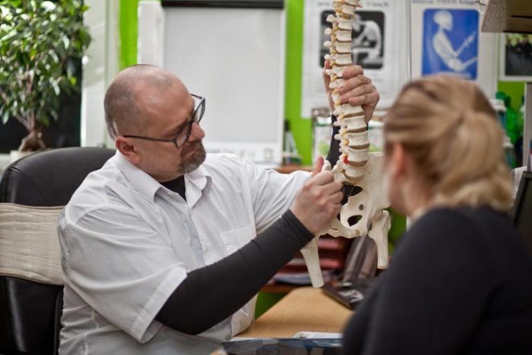 Chiropraktyk pokazuje pacjentce na modelu kręgosłupa źródło bólu krzyża, konsultacja w Poznaniu